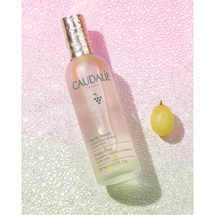 Caudalie Beauty Elixir 100 ml heleyttävä kasvosuihke huurretussa lasipullossa vihreän viinirypäleen rinnalla