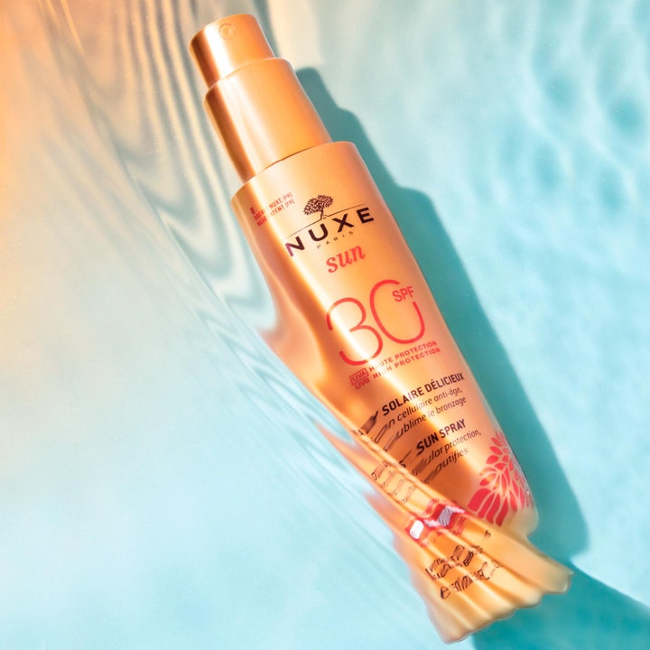 Nuxe Sun Spray SPF30 184 g aurinkovoidetta kasvoille kultaisessa pullossa veden väreilyn keskellä.