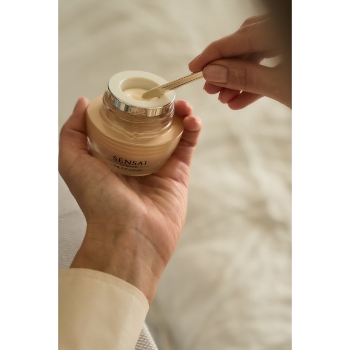 Sensai Ultimate The Eye Cream 15 ml uudistava silmänympärysvoide kultaisessa lasipurkissa spaattelilla annosteltuna