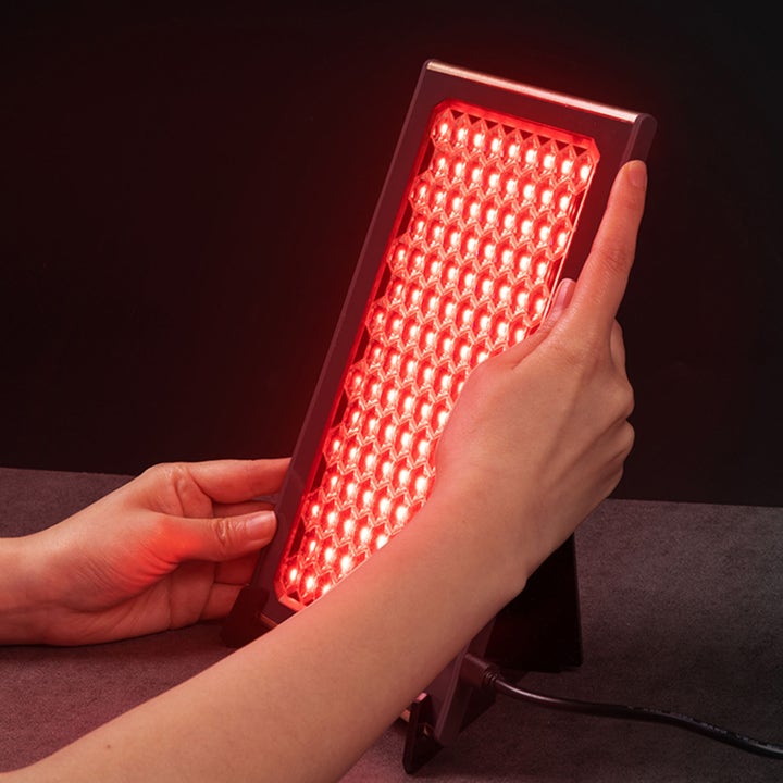 FAQ Swiss FAQ™ Led Panel 1 kpl ihonhoitolaite punaisena hehkuva hunajakennokuvioinen paneeli käsien pitelemänä.