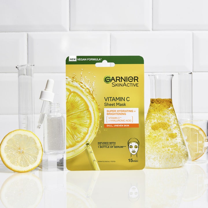 Garnier SkinActive Vitamin C Sheet Mask 28 g kirkastava C-vitamiini kangasmaski sitruunoiden ja laboratoriolasien keskellä.