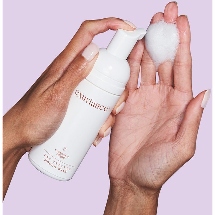 Exuviance Age Reverse BioActiv Wash 125 ml puhdistusvaahto annosteltuna kämmenelle valkoisesta pumppupullosta.
