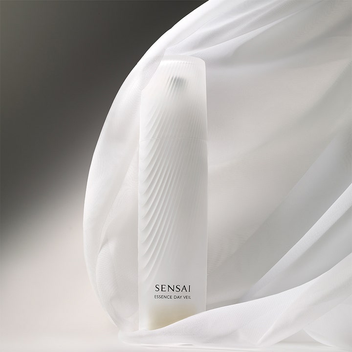 Sensai Essence Day Veil 40 ml suojaava päivävoide aaltoilevassa valkoisessa pullossa ilmavan kankaan ympäröimänä.