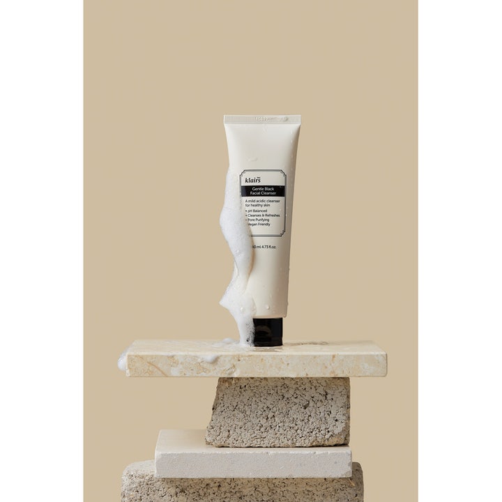 Klairs Gentle Black Facial Cleanser 140 ml puhdistava kasvojenpuhdistusaine valkoisessa tuubissa vaahdon kera kivellä.