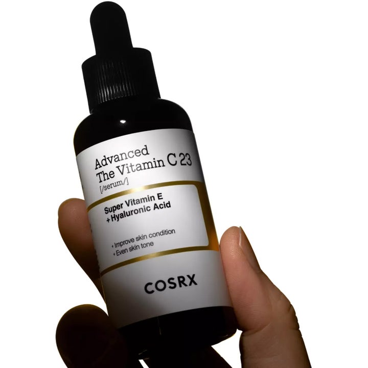 COSRX Advanced The Vitamin C 23 Serum 20 g kirkastava C-vitamiiniseerumi tummassa lasipullossa kädessä pidettynä.