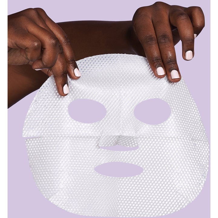 Exuviance Pick-Me-Up Plumping Mask 20 g täyteläistävä sheet mask, jota pidetään käsissä liilan taustan edessä.