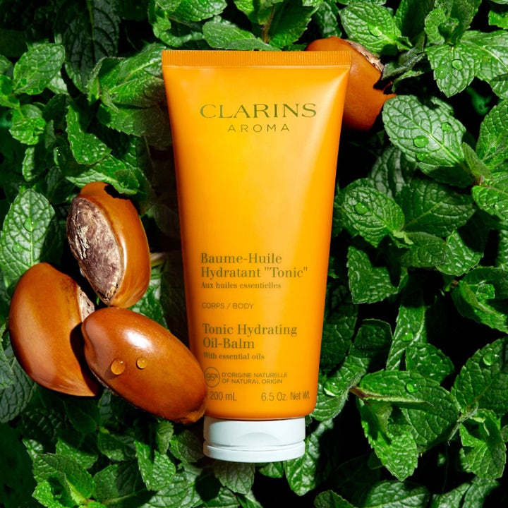 Clarins Hydrating Toning Body Balm 200 ml kosteuttava vartalovoide oranssissa tuubissa mintunlehtien ja pähkinöiden ympäröimänä.
