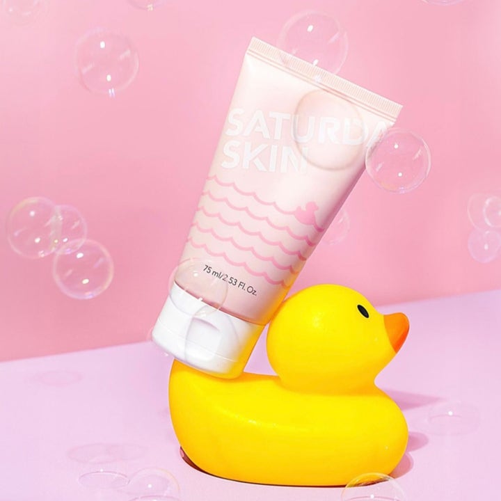 Saturday Skin Rub-a-Dub Refining Peel Gel 75 ml kirkastava kuorinta vaaleanpunaisessa tuubissa kylpyankan päällä.