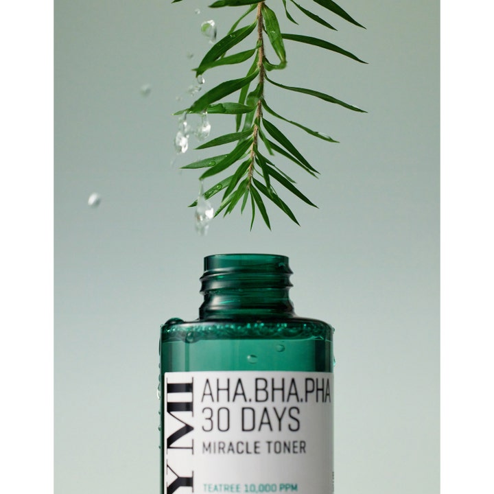 Some By Mi Aha-Bha-Pha 30 Days Miracle Toner 150 ml kuoriva kasvovesi ja teepuun lehtiä vesipisaroilla vihreän pullon yllä.