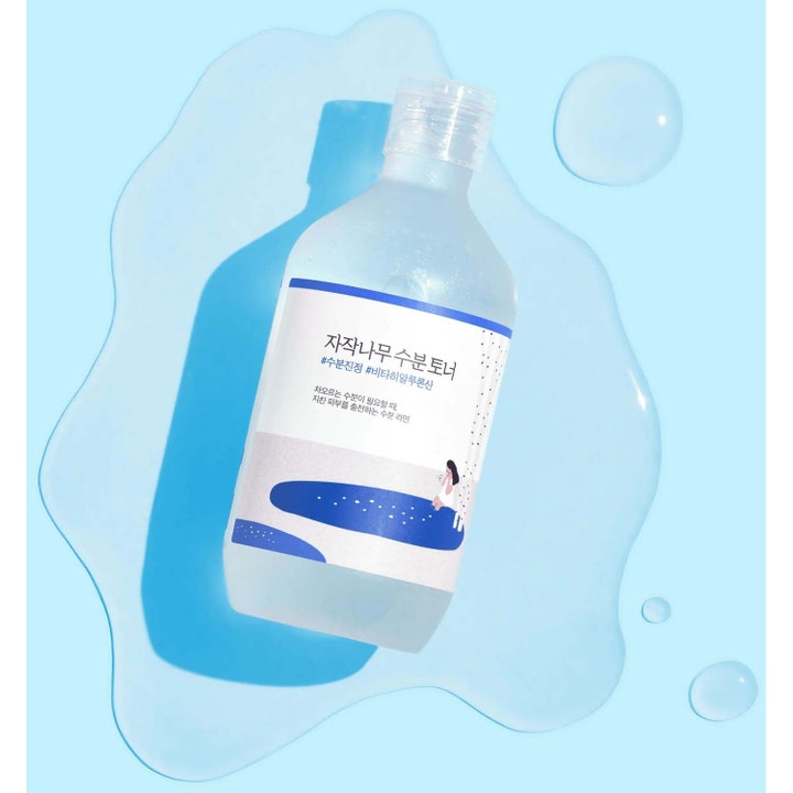 Round Lab Birch Juice Moisturizing Toner 300 ml kosteuttava kasvovesi kirkkaassa pullossa vesilammikoiden ympäröimänä.