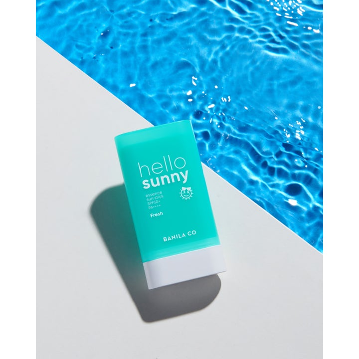 Banila Co Hello Sunny Essence Sun Stick 18,5 g SPF50+ aurinkosuojapuikko turkoosissa hylsyssä uima-altaan reunalla.