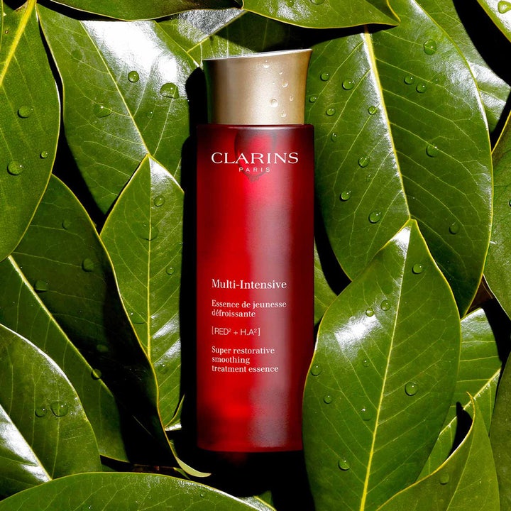 Clarins Super Restorative Treatment Essence 200 ml silottava hoitoneste punaisessa pullossa vihreiden lehtien päällä