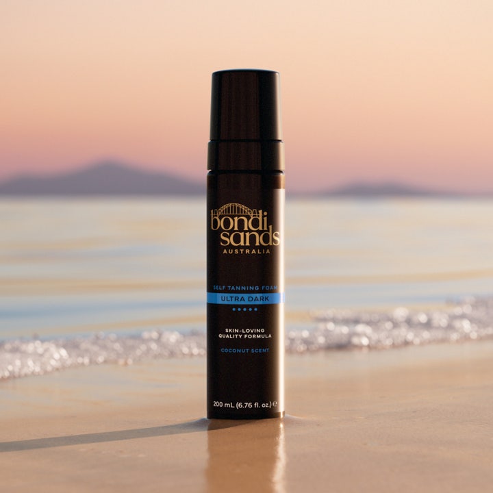 Bondi Sands Self Tanning Foam Ultra Dark 200 ml itsetuskettava vaahto mustassa pullossa hiekkarannalla auringonlaskussa.