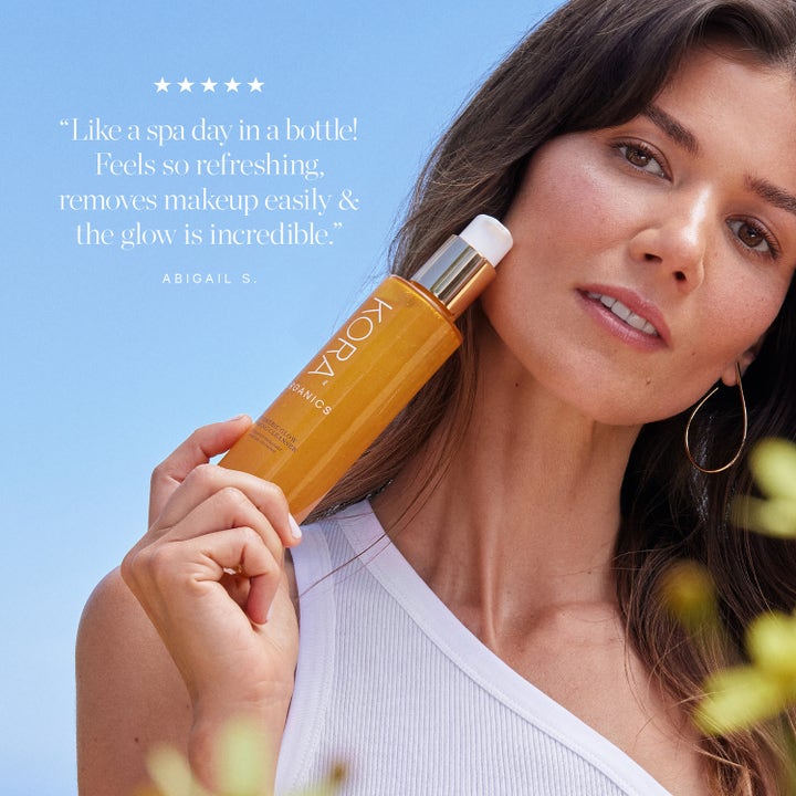 KORA Organics Turmeric Glow Foaming Cleanser 150 ml puhdistusvaahto nainen pitelee pullon poskellaan