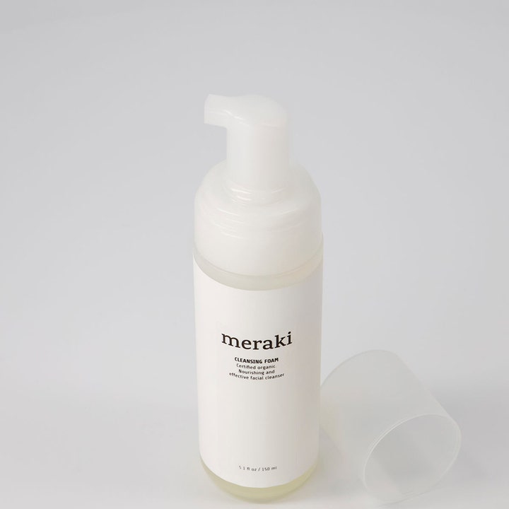 Meraki Cleansing Foam 150 ml ravitseva puhdistusvaahto valkoisessa pumppupullossa, jonka korkki on asetettu viereen.