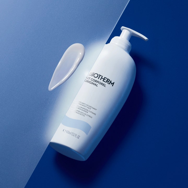 Biotherm Lait Corporel 400 ml kosteuttava vartalovoide valkoinen pumppupullo ja kermainen voidepisara sinisellä pohjalla