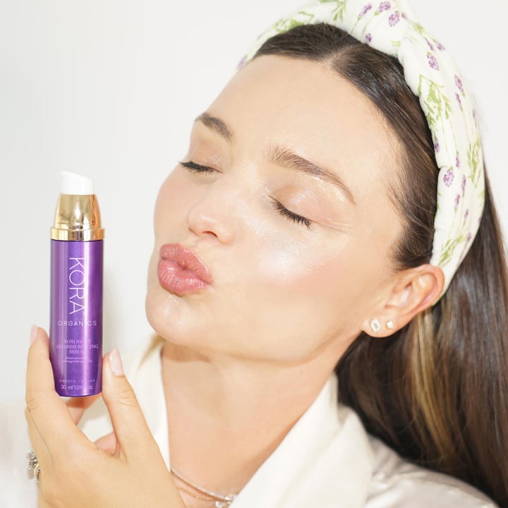 KORA Organics Noni Night AHA Resurfacing Serum 30 ml uudistava AHA-seerumi purppurassa pumppupullossa naisen kädessä.