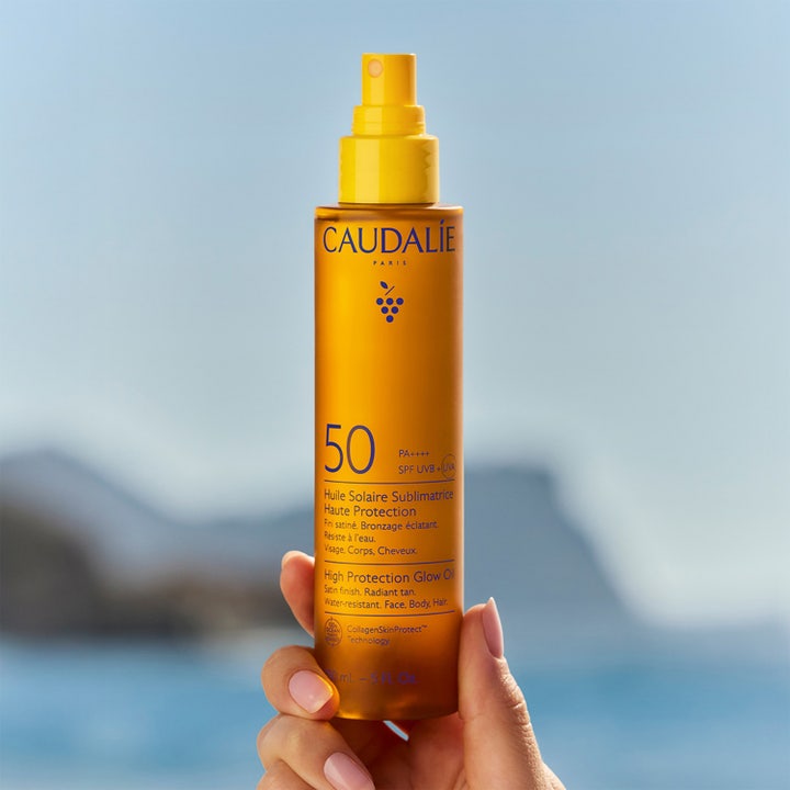 Caudalie Vinosun High Protection Glow Oil 150 ml SPF50 aurinkosuojaöljy oranssissa pullossa rantamaisemassa.