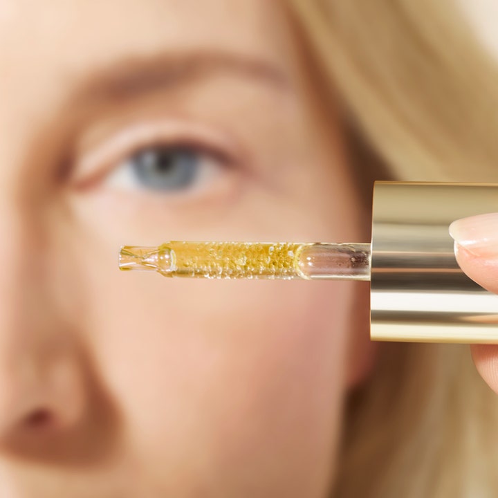 Nuxe Super Serum [10] Eye 15 ml kirkastava silmänympärysseerumi ja pipetti täynnä kultaisia öljyhelmiä.