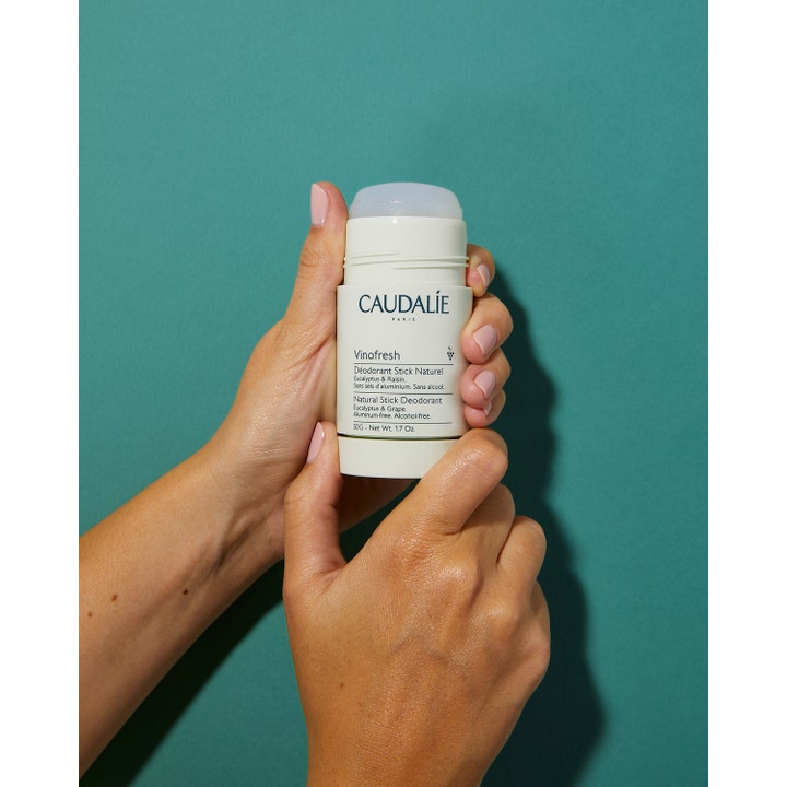 Caudalie Vinofresh Stick Deodorant 50 ml alumiiniton deodorantti valkoisessa hylsyssä käsissä vihreällä taustalla.