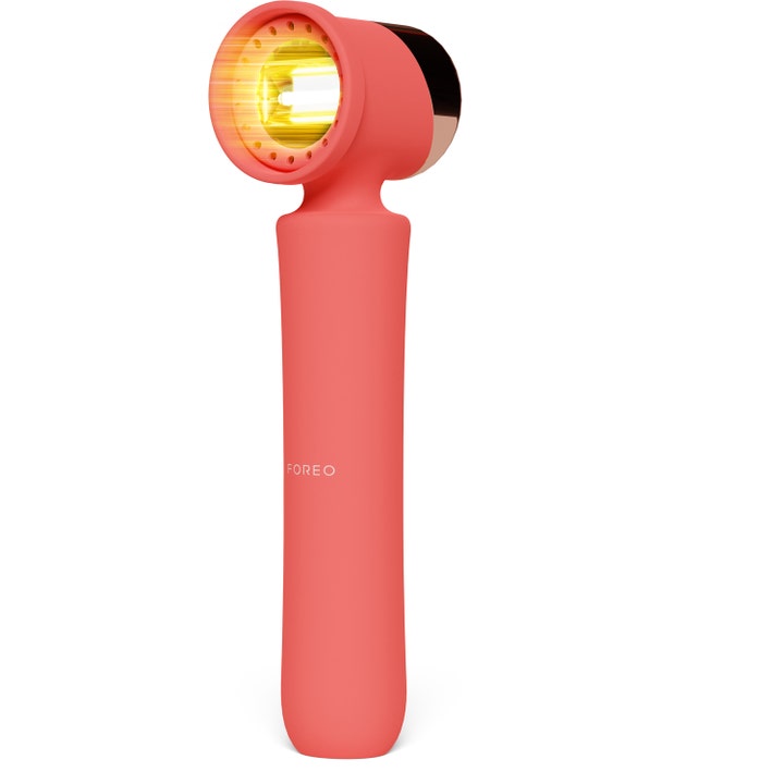 Foreo FAQ 211 hiuspohjaa vahvistava LED-laite on persikanvärinen ja siinä on hehkuva keltaisen oranssi valo.