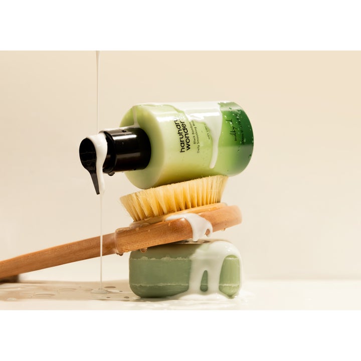 Haruharu Wonder Black Bamboo Daily Smoothing Body Oil 200 ml vartaloöljy valuu vihreän pullon ja pesuharjan päälle.