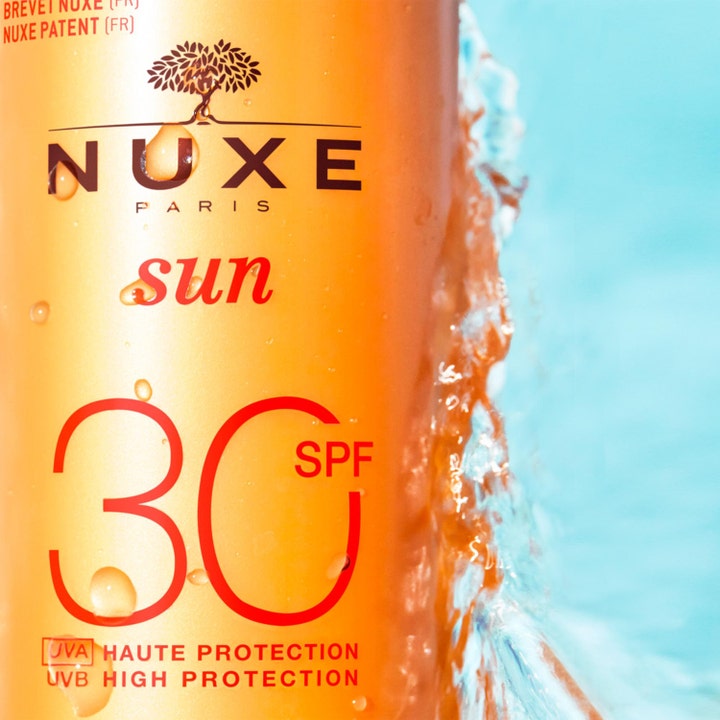 Nuxe Sun Spray SPF30 184 g aurinkosuojasuihke antaa korkean suojan oranssissa pullossa vesiroiskeiden keskellä.