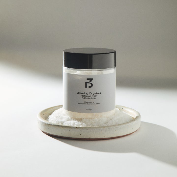 Bodyologist Calming Crystals 250 g rentouttava kylpysuola mustakantisessa purkissa keraamisella alusella.