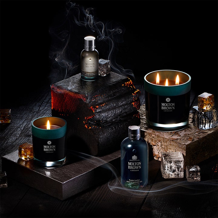 Molton Brown Dark Leather Bath & Shower Gel 300 ml suihkugeeli hehkuvan puun ja savuisten kynttilöiden ympäröimänä.