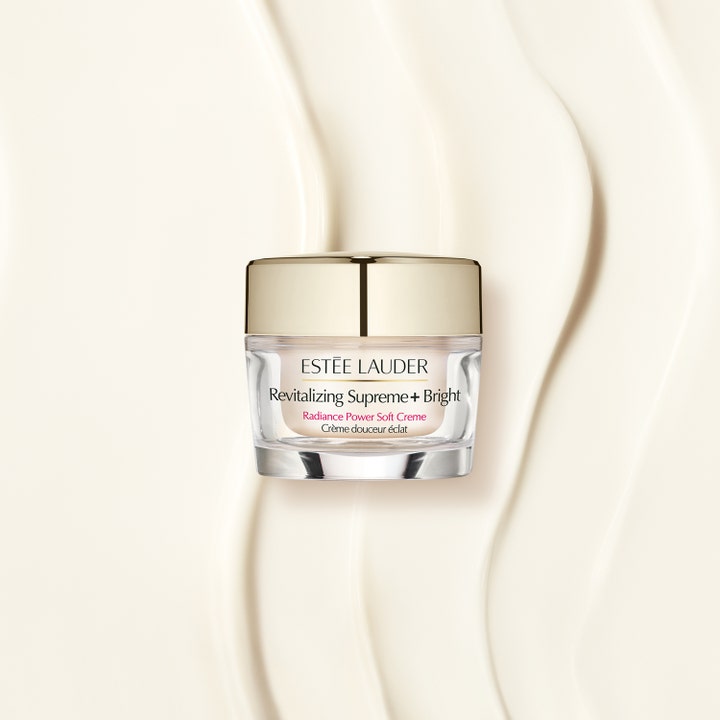 Estée Lauder Revitalizing Supreme+ Bright 50 ml heleyttävä kasvovoide kultakantisessa lasipurkissa voidemaisella taustalla.