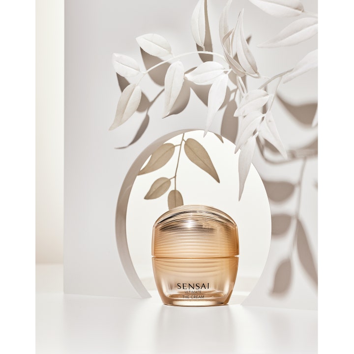 Sensai Ultimate The Cream 40 ml uudistava kasvovoide kultaisessa lasipurkissa valkoisten lehtien ympäröimänä.