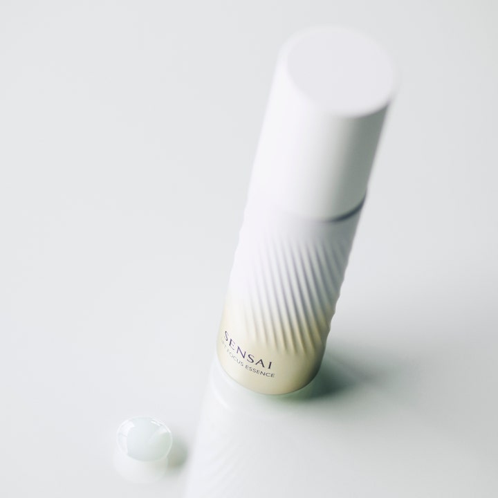 Sensai Lift Focus Essence 40 ml kiinteyttävä seerumi uritetussa valkokultaisessa pullossa ja pisara koostumusta