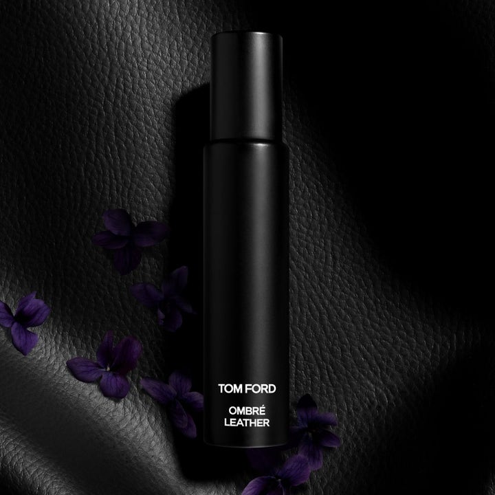 Tom Ford Ombré Leather tuoksu tyylikkäässä mustassa pullossa mustan nahan ja violettien kukkien keskellä