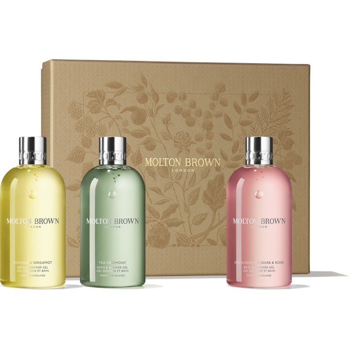 Molton Brown Bath & Shower Gel 3 x 300 ml puhdistava lahjasetti sisältää kolme värikästä pulloa kultaisen rasian edessä.