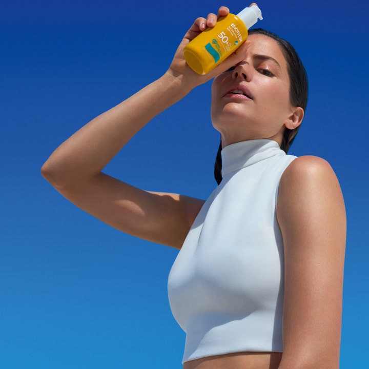 Biotherm Waterlover Sun Milk 200 ml aurinkosuojavoide SPF 50 nainen pitelee keltaista pulloa sinistä taivasta vasten