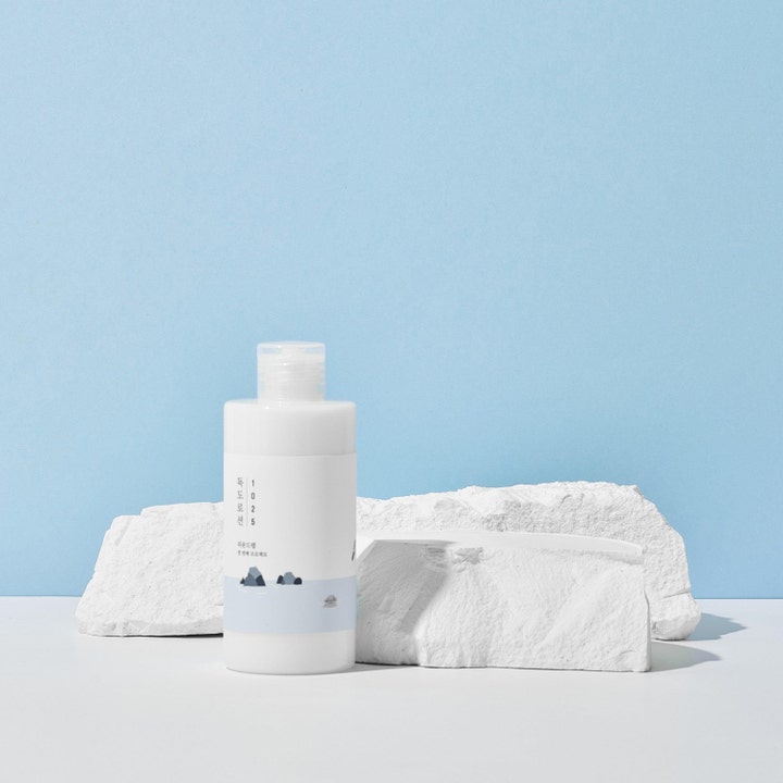 Round Lab 1025 Dokdo Toner Lotion Special Set 400 ml kosteuttava voide valkoisessa pullossa vaaleiden kivien edessä.