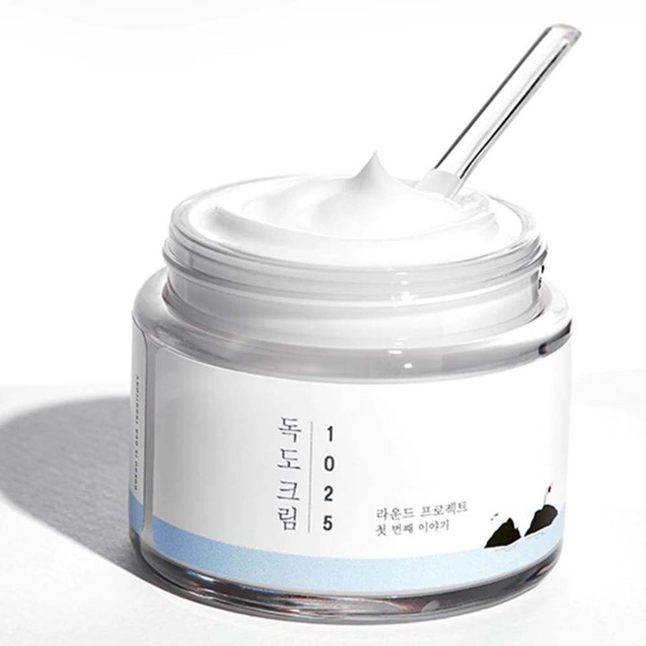 Round Lab 1025 Dokdo Cream 80 ml kosteuttava kasvovoide avatussa purkissa, jossa on täyteläistä voidetta ja spaatteli.