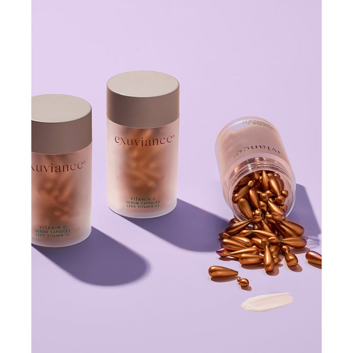 Exuviance Vitamin C Serum Capsules 60 kpl heleyttävä seerumi ja pronssisia kapseleita valumassa ulos purkista.