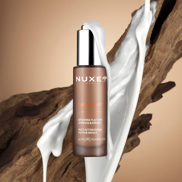 Nuxe Men Multi Action Serum 30 ml energisoiva seerumi ruskeassa pullossa valkoisen koostumuksen valuessa puun päällä