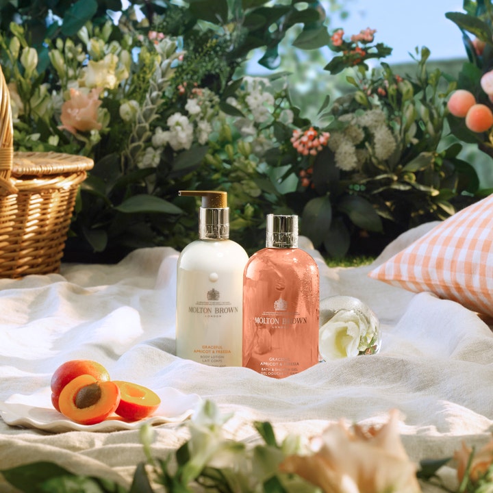 Molton Brown Graceful Apricot & Freesia Body Lotion 300 ml kosteuttava vartalovoide valkoisessa pumppupullossa piknikillä.