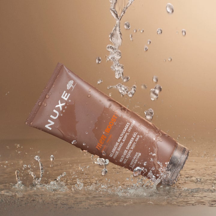 Nuxe Men Multi Shower Gel 200 ml puhdistava suihkugeeli ruskeassa tuubissa dynaamisten vesiroiskeiden keskellä.