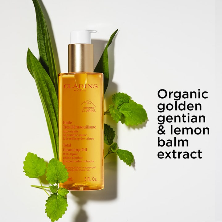 Clarins Total Cleansing Oil 150 ml puhdistusöljy kultaisessa pullossa vihreiden lehtien ympäröimänä.