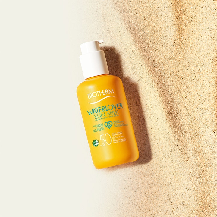 Biotherm Waterlover Sun Milk SPF50 200 ml suojaava aurinkovoide keltaisessa pumppupullossa hiekalla.