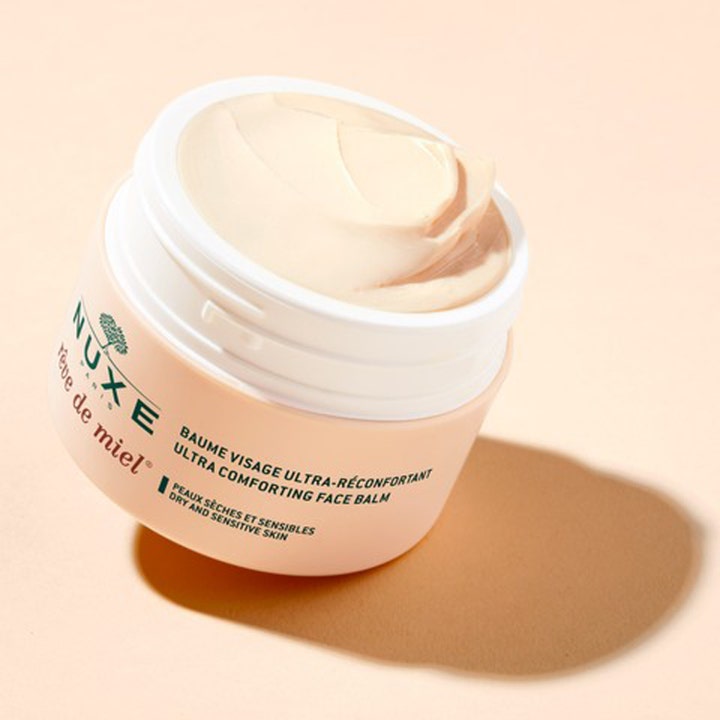 Nuxe Rêve de Miel 50 ml ravitseva kasvovoide, jonka täyteläinen vaalea voide näkyy avatussa persikanvärisessä purkissa.
