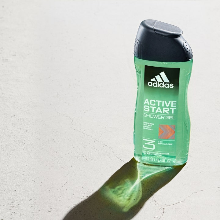 Adidas Active Start 250 ml 3-in-1 suihkugeeli virkistää ihoa vihreässä läpinäkyvässä pullossa harmaalla pinnalla.