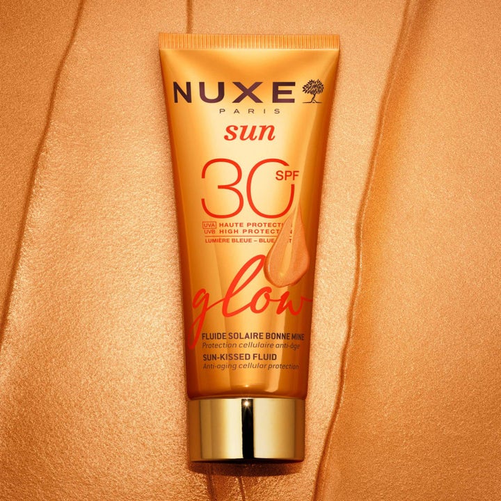 Nuxe Sun-Kissed Fluid 40 ml heleyttävä SPF 30 aurinkovoide oranssissa tuubissa kimaltavalla pronssisella taustalla.