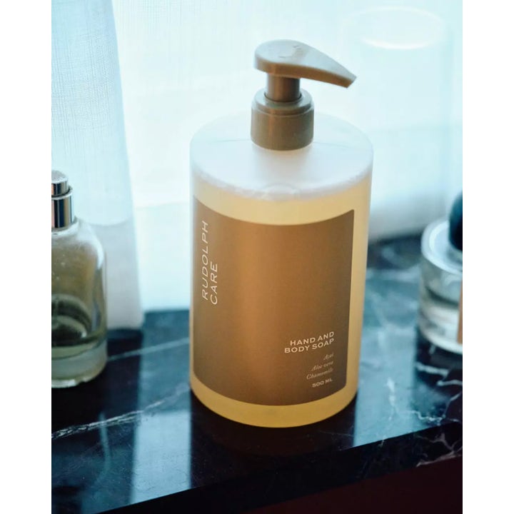 Rudolph Care Hand And Body Soap 500 ml puhdistava suihkusaippua beigellä etiketillä ja pumpulla marmorilla
