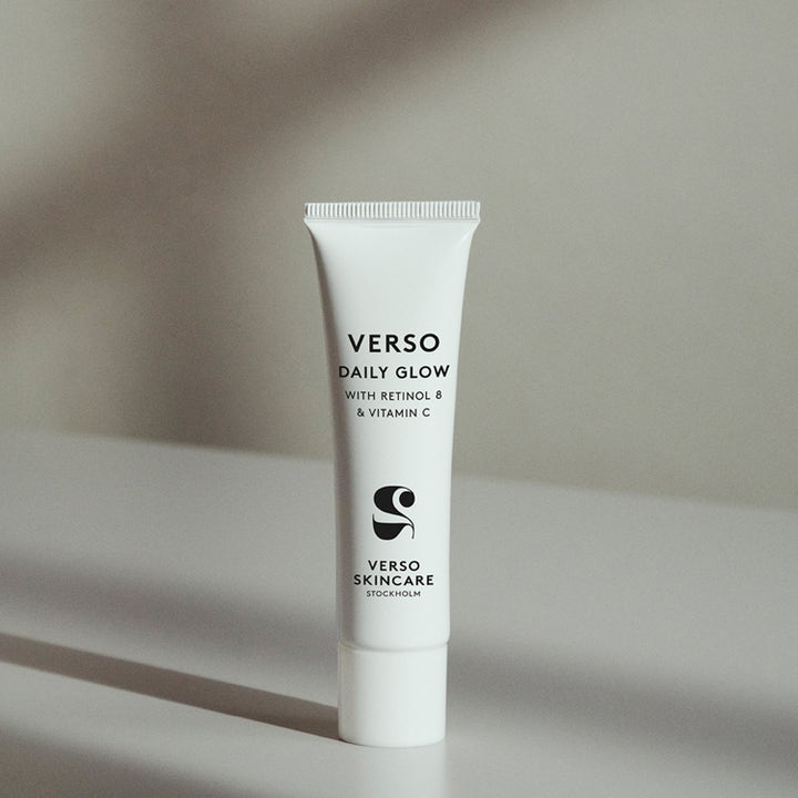 Verso Daily Glow With Retinol 8 &amp; Vitamin C 30 ml kirkastava seerumi valkoisessa tuubissa pehmeiden varjojen keskellä.