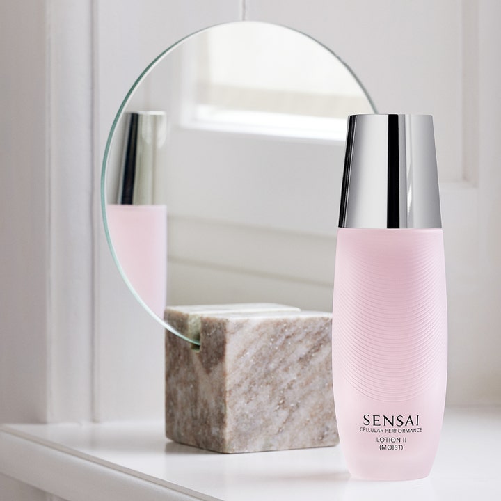Sensai Cellular Performance Lotion II Moist 125 ml kosteuttava kasvovesi vaaleanpunaisessa pullossa peilin edessä.