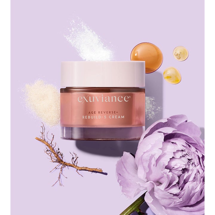 Exuviance Age Reverse + Rebuild-5 Cream 50 ml silottava päivävoide lasipurkissa kukkien ja jauheen ympäröimänä.